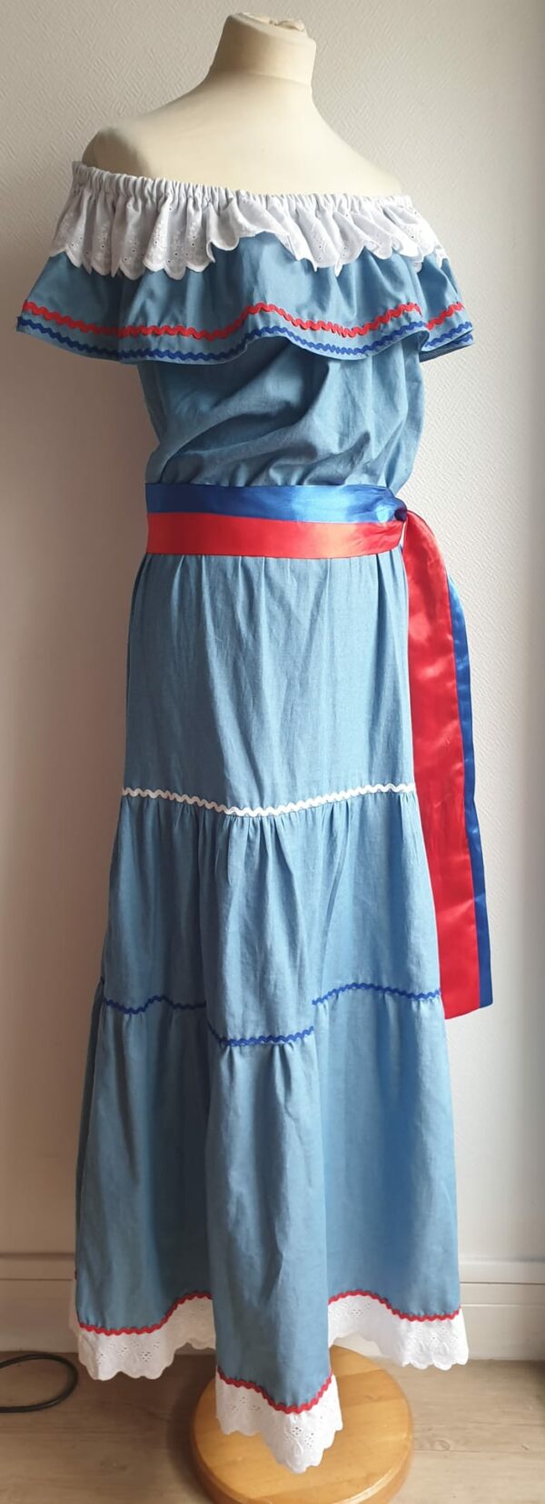 Robe carabela haïtienne longue, de couleur bleue claire et fournie avec 2 ceintures. Elastique à la taille.