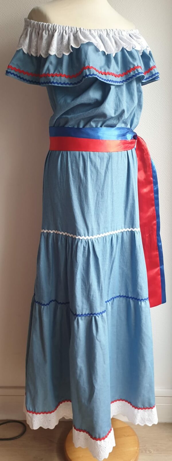 Robe carabela haïtienne longue, de couleur bleue claire et fournie avec 2 ceintures. Elastique à la taille.