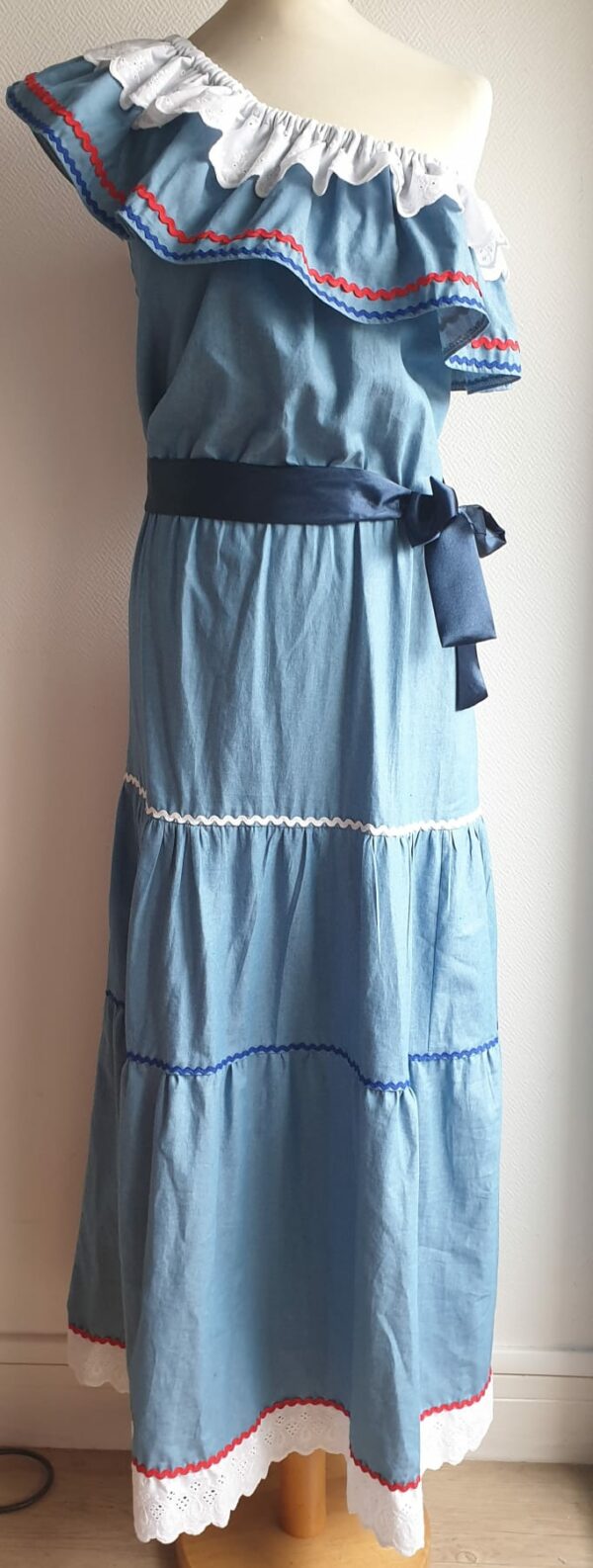 Robe carabela haïtienne longue, de couleur bleue claire et fournie avec 2 ceintures. Elastique à la taille.