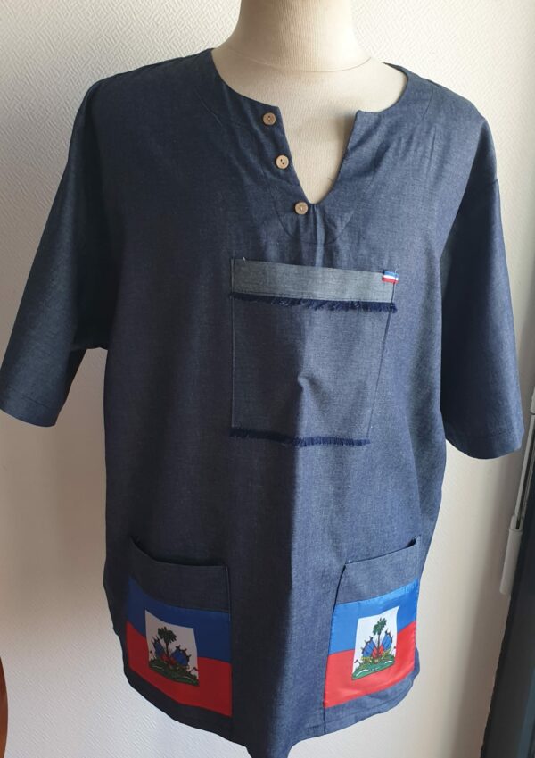 Chemise de couleur bleue foncée assortie du drapeau Haïti sur les deux des trois poches principales, sur une tenue traditionnelle. Une poche miniature supplémentaire a été autorisée sur l'une des deux manches courtes. Une série de trois petits boutons en bois clair est disposée prés le col en V. Le tissu est en carabela pur coton cent pour cent. Taille : S M L XL XXL. Prix : 79.95€ . Cette chemise est confectionnée à Paris par Anjero.