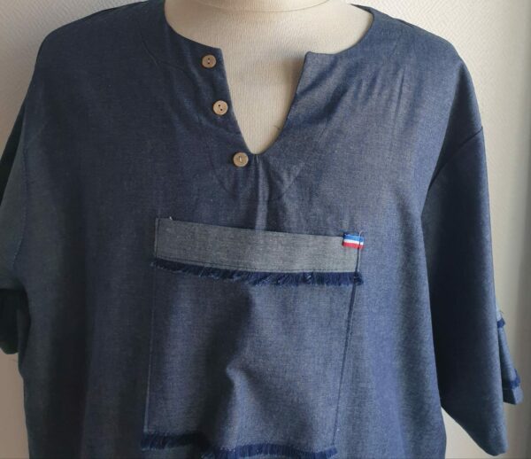 Chemise de couleur bleue foncée assortie du drapeau Haïti sur les deux des trois poches principales, sur une tenue traditionnelle. Une poche miniature supplémentaire a été autorisée sur l'une des deux manches courtes. Une série de trois petits boutons en bois clair est disposée prés le col en V. Le tissu est en carabela pur coton cent pour cent.