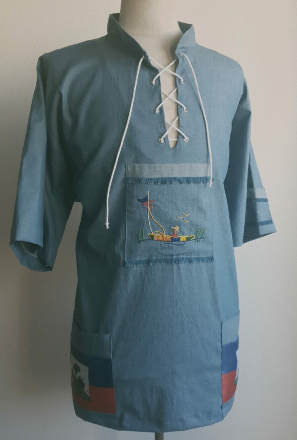 113.1Chemise bleue carabela en tenue traditionnelle haïtienne brodée à la main. Deux poches latérales, une poche brodée centrale, une mini poche sur une manche courte. Taille : S M L XL XXL. Made in Paris et confectionnée par Anjero. Prix : 94,95€