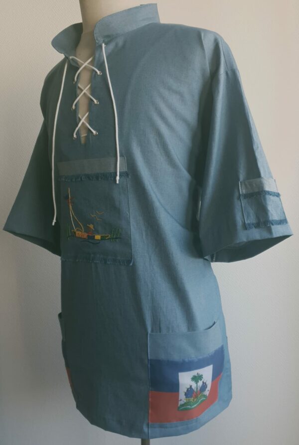 Chemise bleue carabela en tenue traditionnelle haïtienne brodée à la main. Deux poches latérales, une poche brodée centrale, une mini poche sur une manche courte.