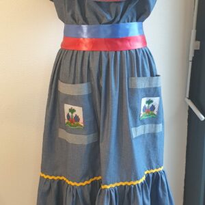 13.1Robe Carabela cintrée sur un fond bleu et sur une tenue traditionnelle haïtienne. Deux poches sur le devant de la robe avec le petit drapeau. Cette robe est conçu pour être élastique à la taille. Elle est aussi garnie de serpentines aux couleurs vives et elle est livrée avec une ceinture bicolore au drapeau haïtien. Taille : S, M, L, XL, XXL. Prix : 159€. Créateur Anjero.