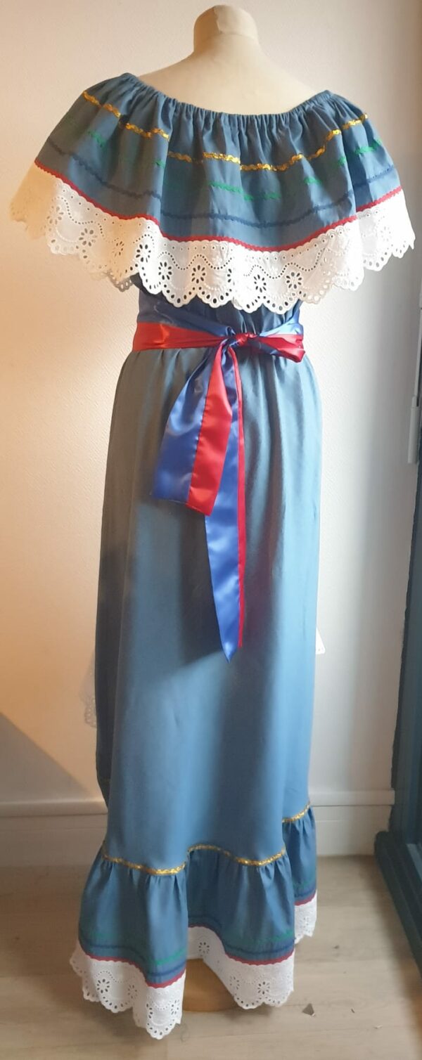 Robe Carabela cintrée sur fond bleu et sur une tenue traditionnelle haïtienne pour cérémonie, mariage, gala, baptême. Une finition au col de la robe et sur son bas de jupe est brodé en dentelles anglaises. Des serpentines aux quintuples couleurs or, vert, jaune, rouge et blanc; Une ceinture aux couleurs du drapeau haïtien; Un tissu cent pour cent coton; Une souplesse à la taille à laquelle est intégré un élastique sont autant de particularités qui confèrent à la confection toute son originalité. Made in Paris. Créé par Anjero.