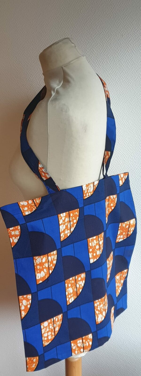 2.3Tote-bag Wax imprimé sur fond bleu et motifs de couleur vive. Additionné d'un bandeau assorti sur un lot de 2 pièces. Création Anjero.